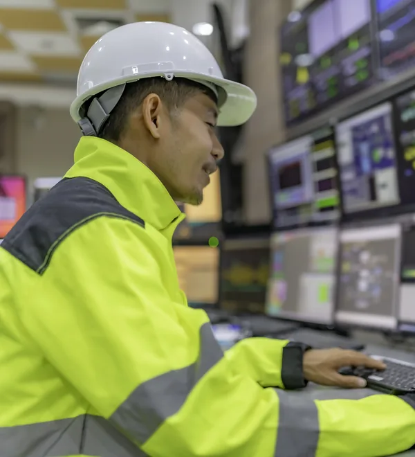 Engineer in a hard hat watching plant readings across a wall of control room screens