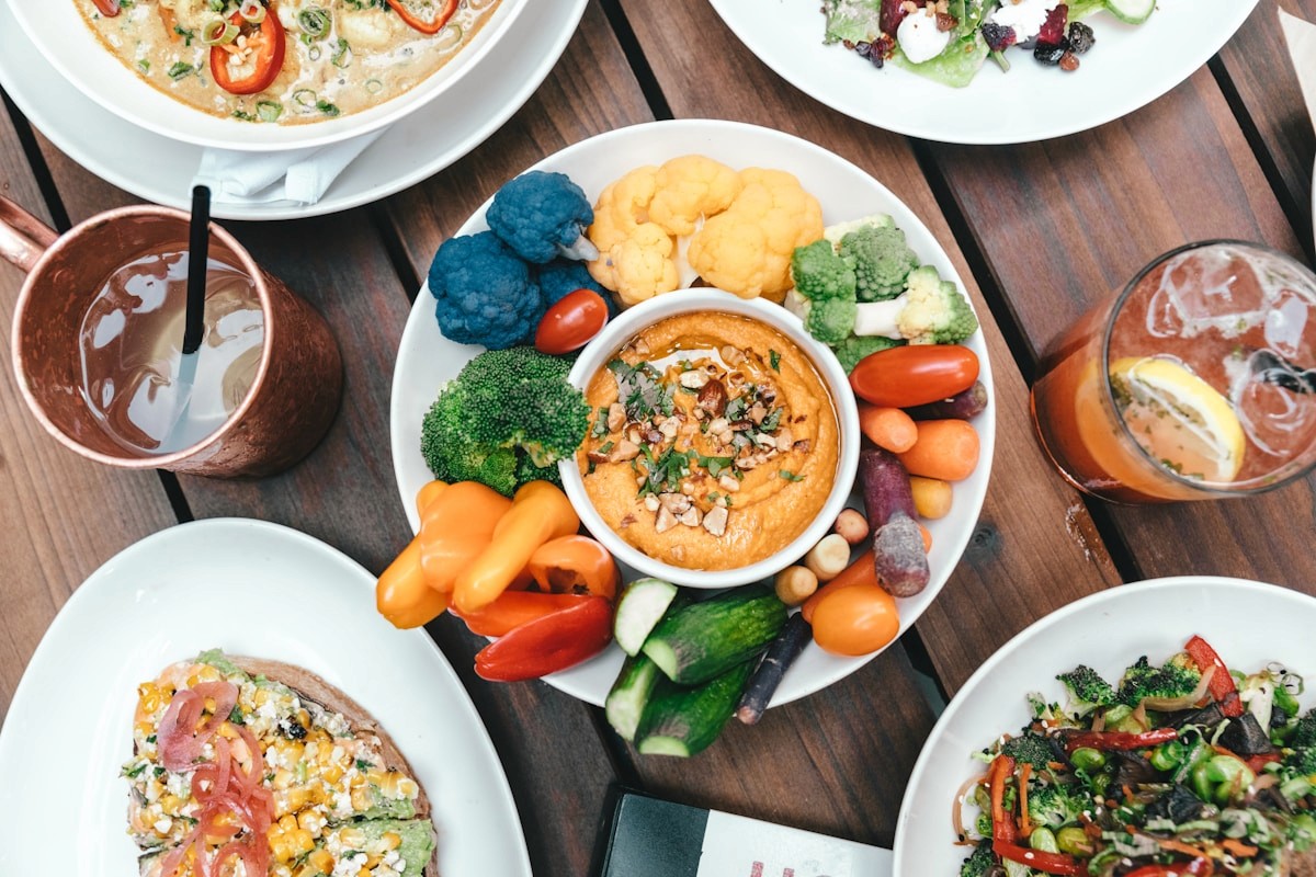 A balanced plate of fresh vegetables with a creamy dip surrounded by other dishes, showing how all foods fit in a recovery meal plan