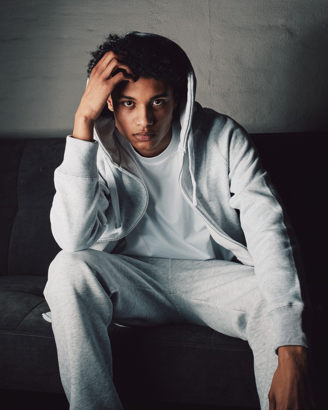Person wearing light grey sweatsuit in a dark room