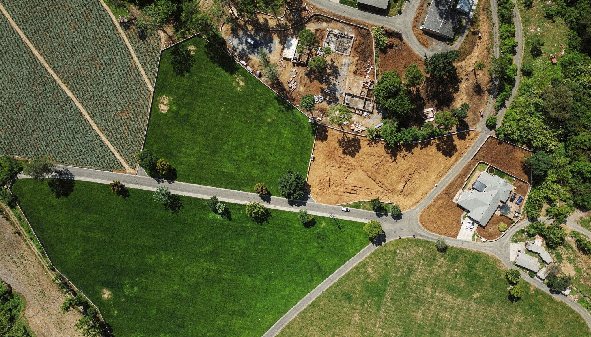 An aerial view looking down at a row of metal grain silos standing next to a lush green cornfield on a sunny day.