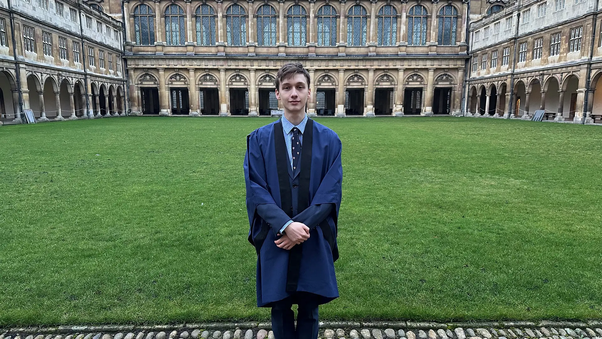 Jakub v univerzitním plášti na vnitřním nádvoří Trinity College s výhledem na arkády a historickou architekturu.