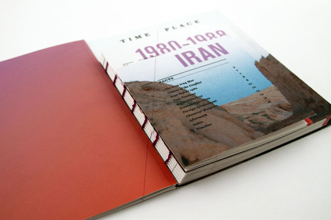 The image shows an open book resting on a white surface. The book's cover is predominantly white with the text "TIME PLACE 1980-1990 IRAN" prominently displayed in purple letters. A photograph of a mountainous landscape with a blue-gray sky is featured on the cover. The spine of the book is visible, revealing a reddish-orange cover. The book is positioned diagonally, with the open pages facing upwards. The background is a plain white surface.