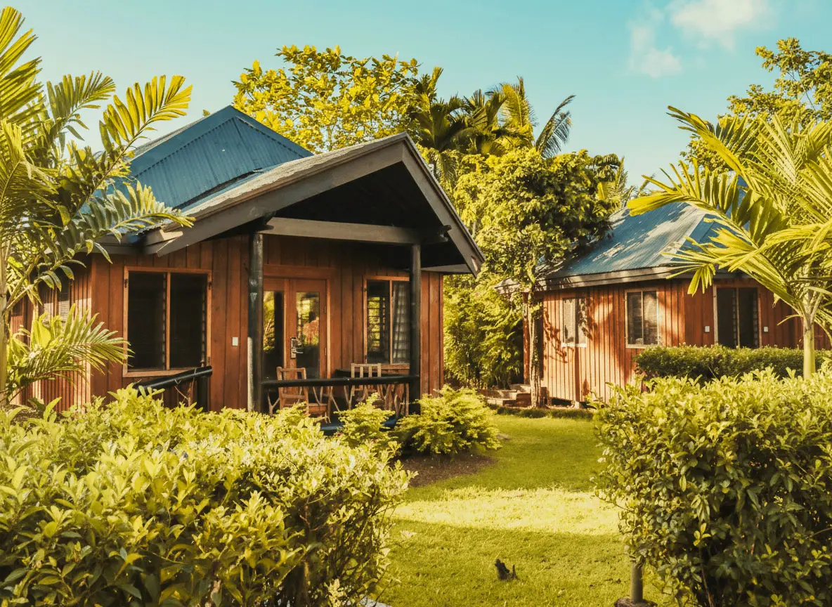 Two traditional Fiji bures with dark roofs nestled amidst lush tropical greenery at Uprising Beach Resort.
