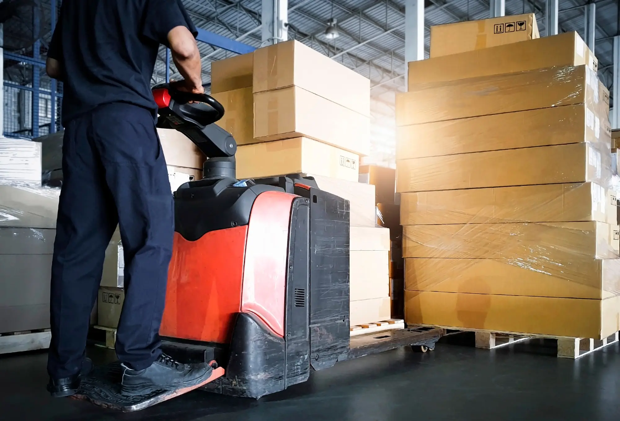 Warehouse worker moving stacked boxes with an electric pallet jack