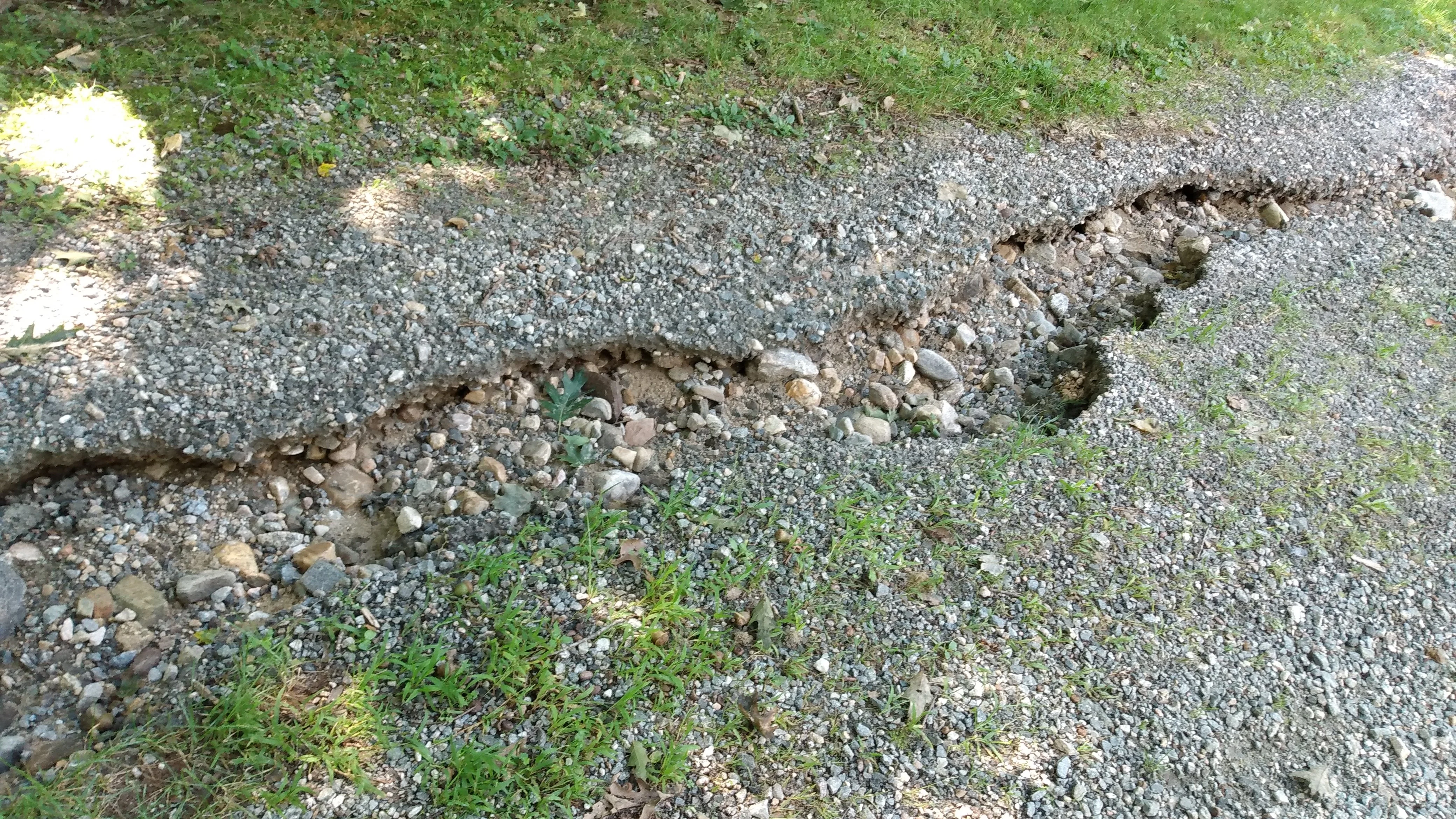Gravel driveway edge failure showing aggregate mixing with soil due to lack of geotextile separation.