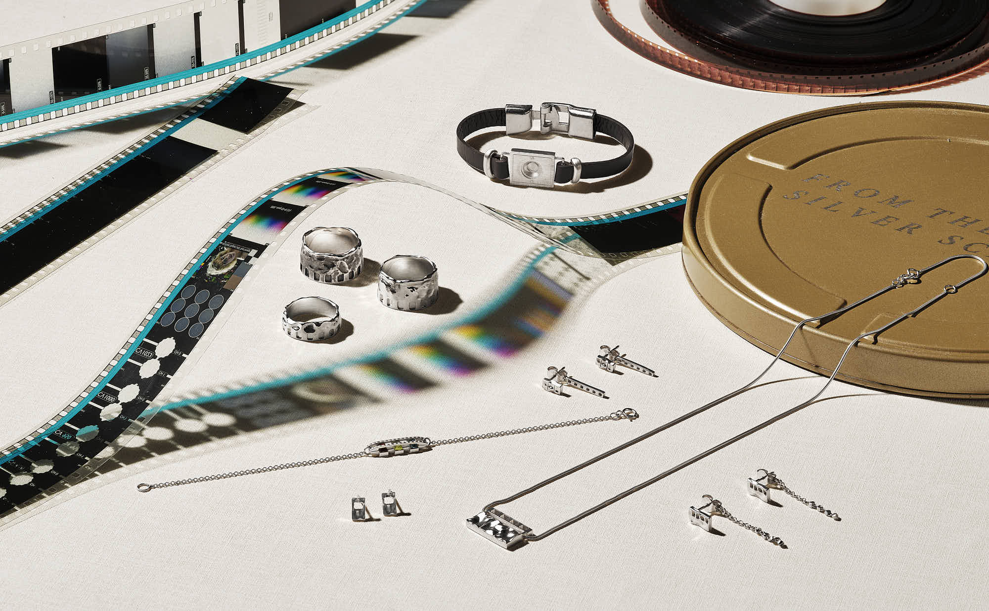 Unique silver jewelry set with film reels and vintage camera accessories on a textured surface.