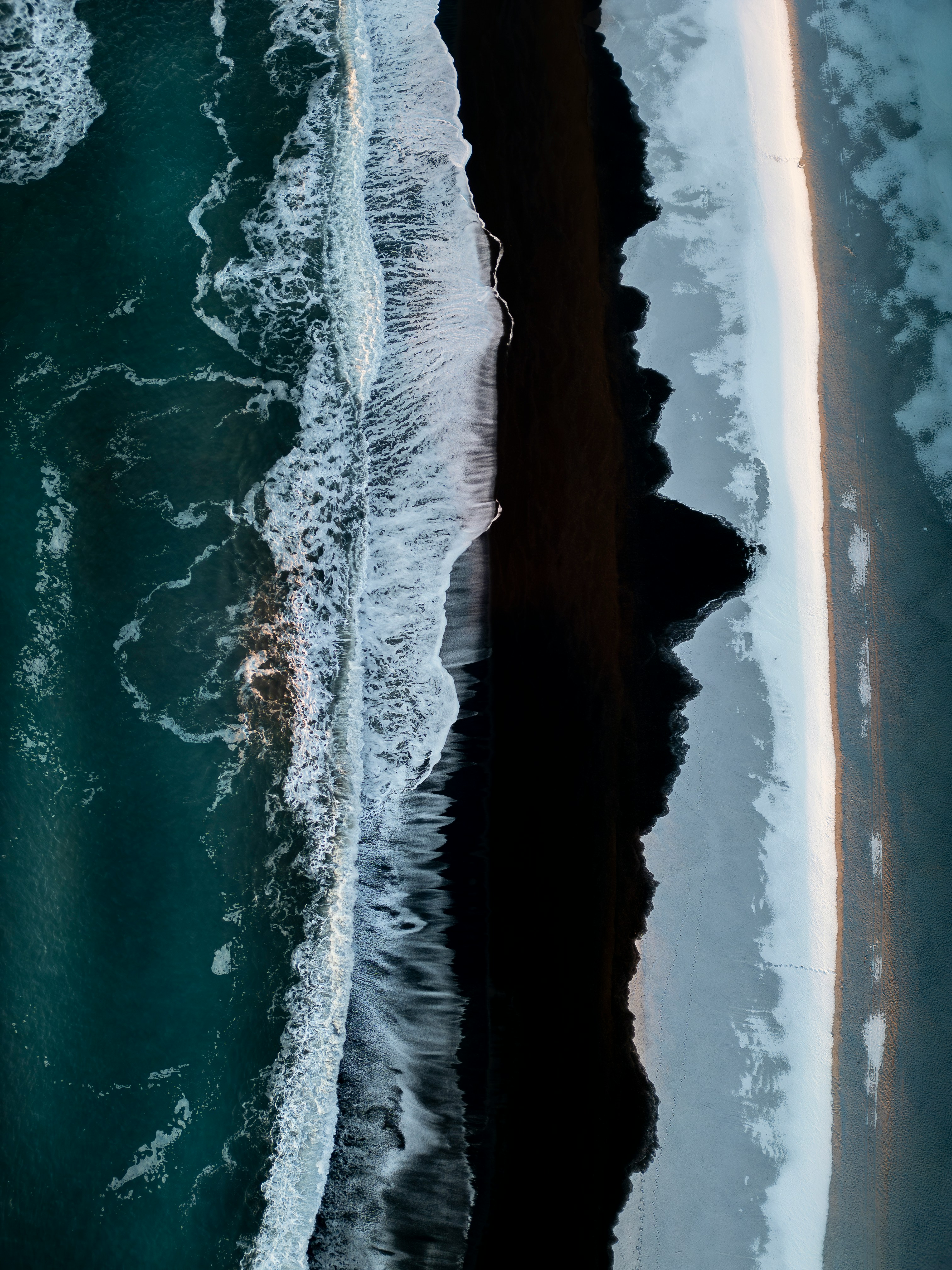 Aerial view of waves crashing on a black sand beach