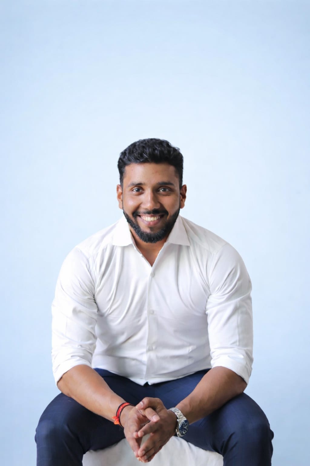 A smiling man with curly hair is sitting at a desk, looking at the camera, with a laptop and a lamp in the background.