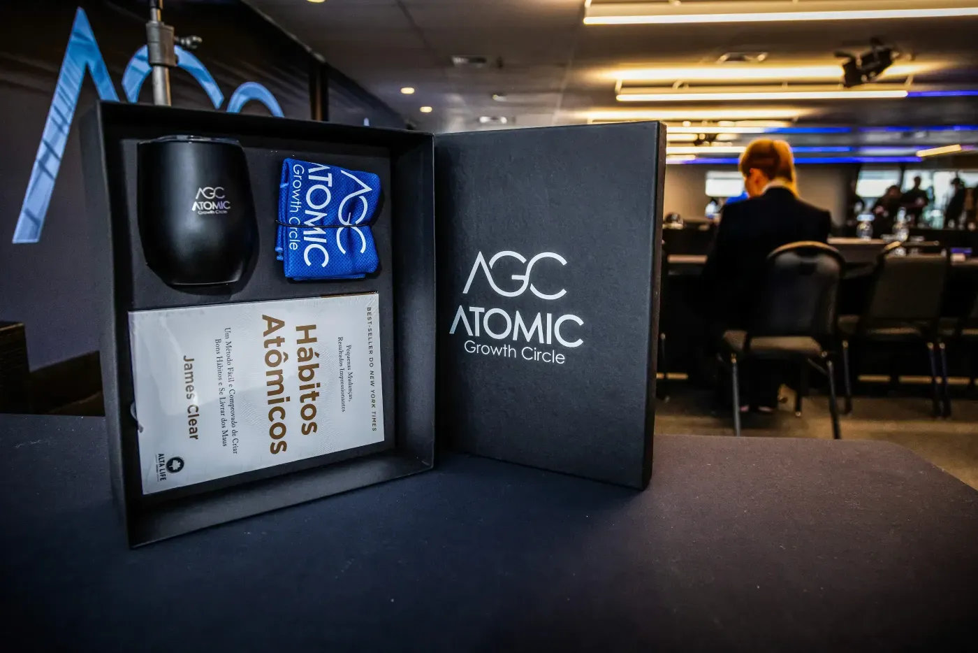 A modern display setup featuring digital screens and a booth labeled "AGC ATOMIC GROWTH CLUB," in a professional environment. Atomic Growth Club. Atomic Group. Br24. 