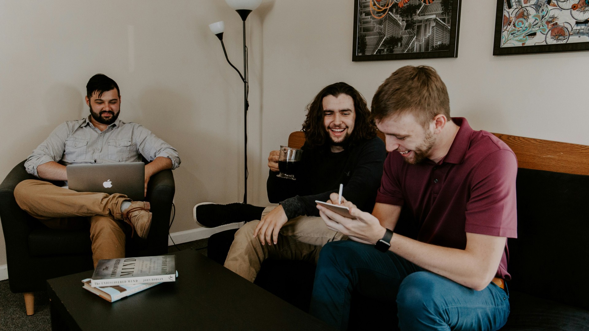 Three people sitting on a couch in a room looking at mobile devices