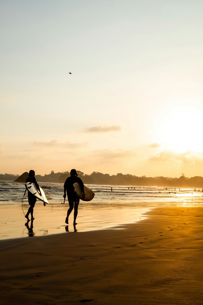 Two surfers walk on beach at sunset