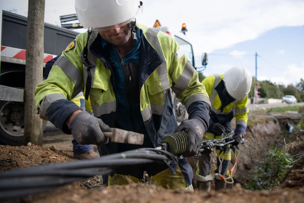 Techniciens en gilet haute visibilité posant des câbles souterrains fibre optique en tranchée sur chantier