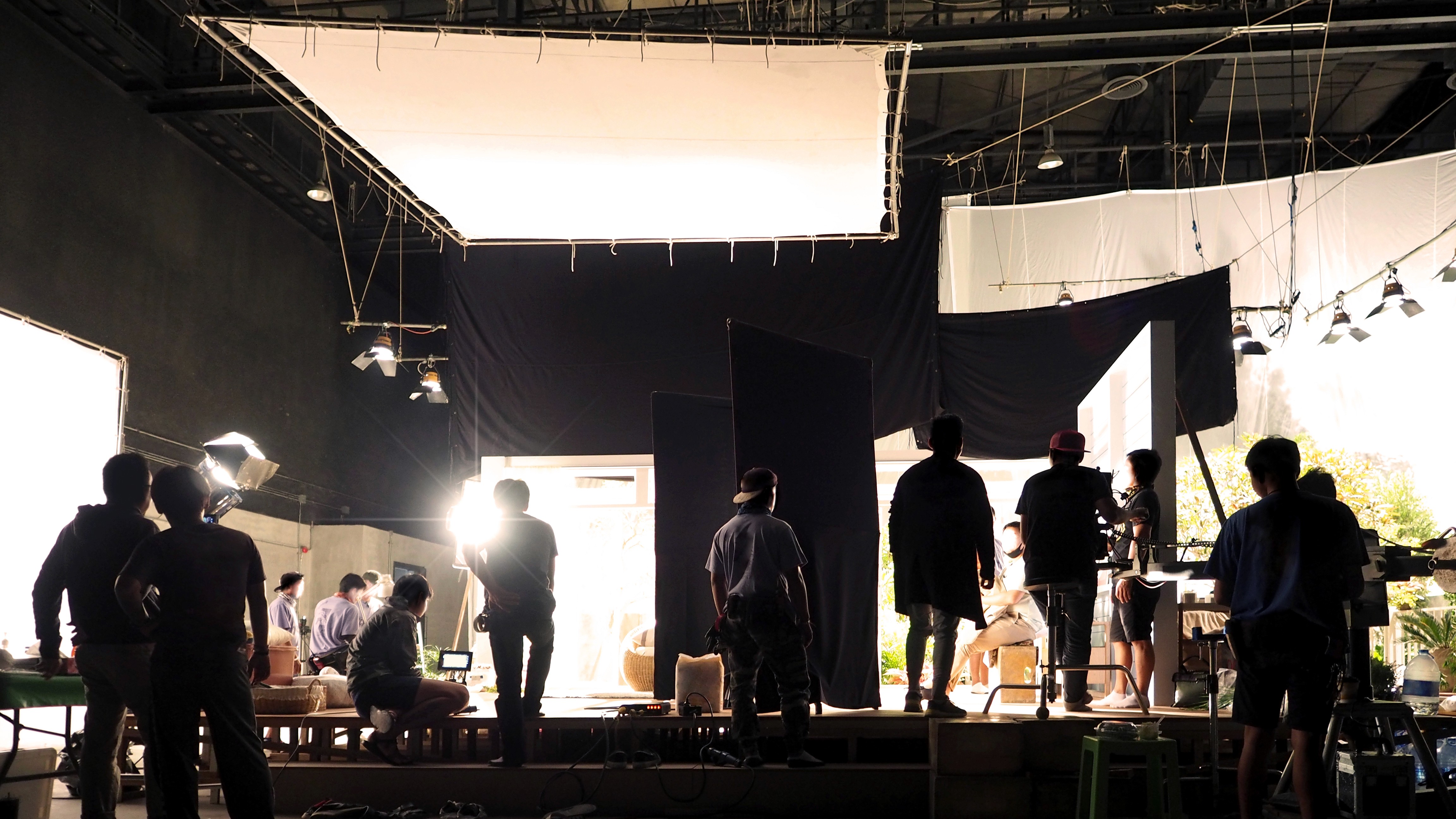 Film crew working on a studio set with lighting rigs, grips, and technicians preparing the scene—representing cinematographers, gaffers, key grips, and production teams.