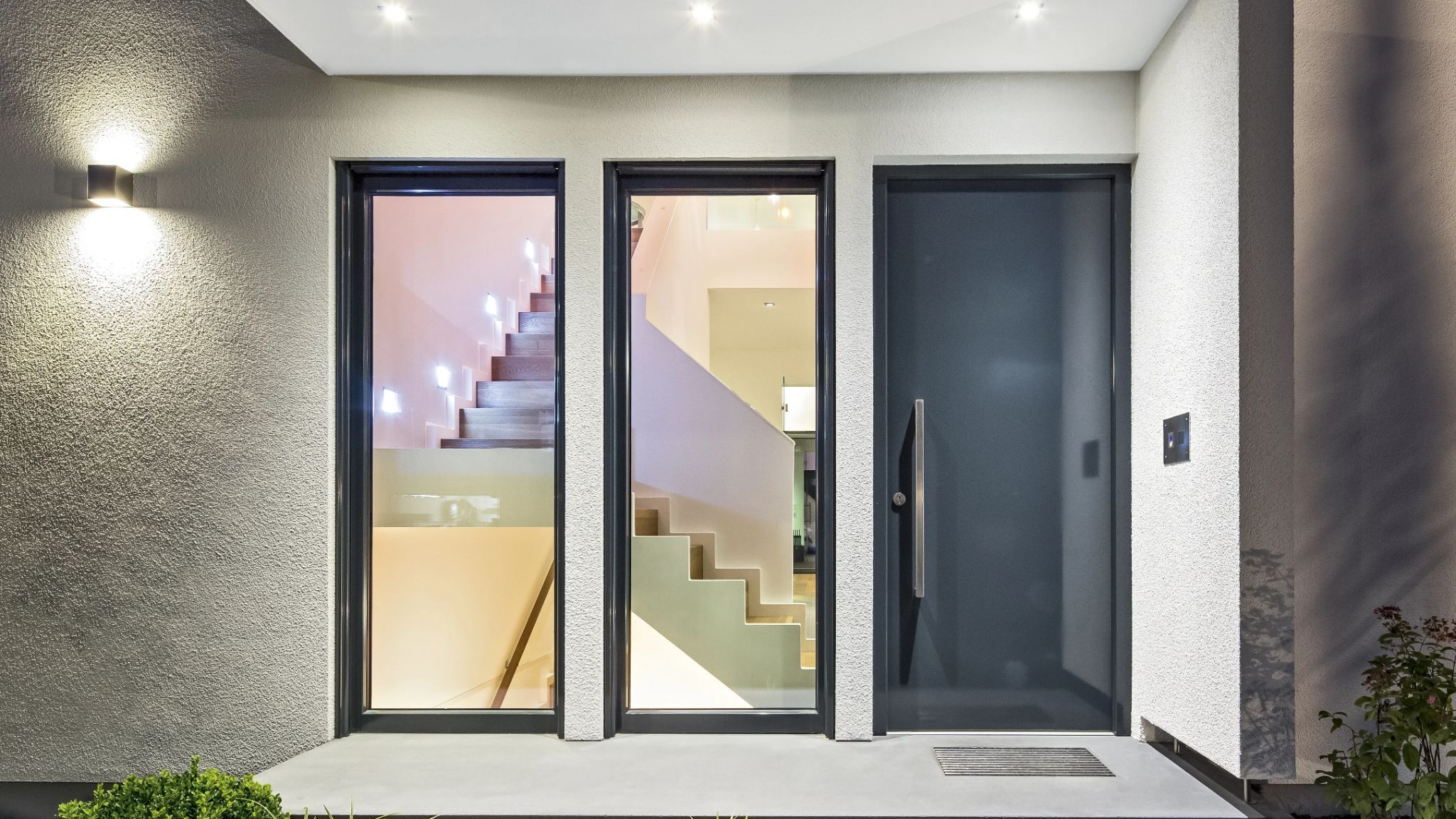 Moderne Hauseingangstür mit integrierten Glaselementen, die den Blick auf eine elegante Treppe freigeben.
