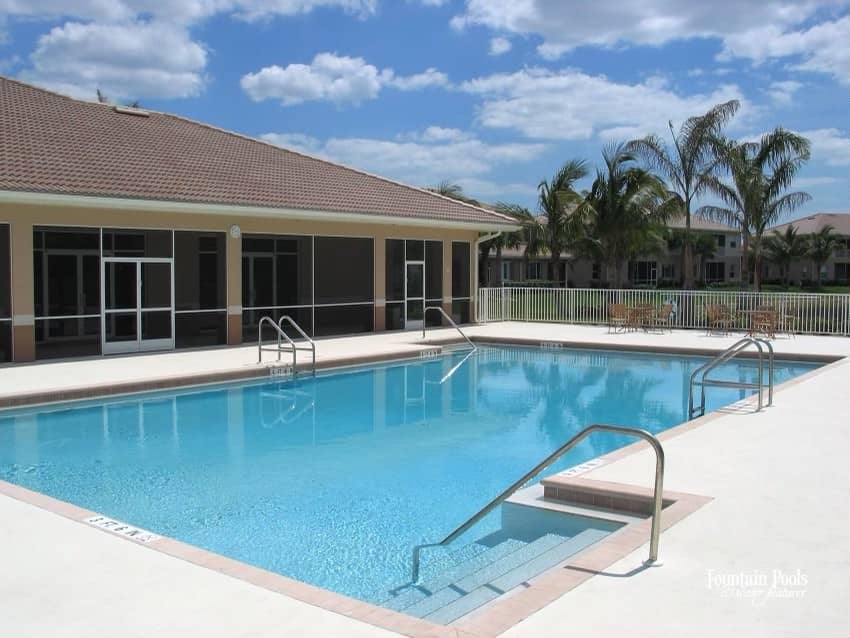 Image of residential pool with accessible entrances around the perimeter of the pool, including a pool deck. Tan house with red roof in the background.