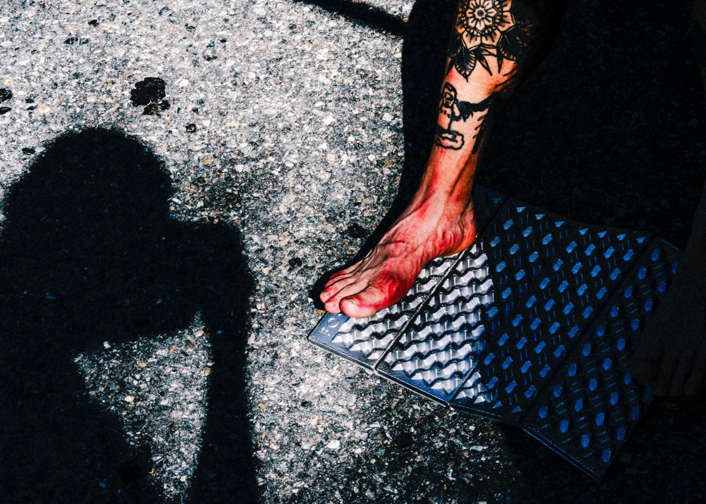 Tattooed bare foot on a camping mat beside a runner shadow on the asphalt