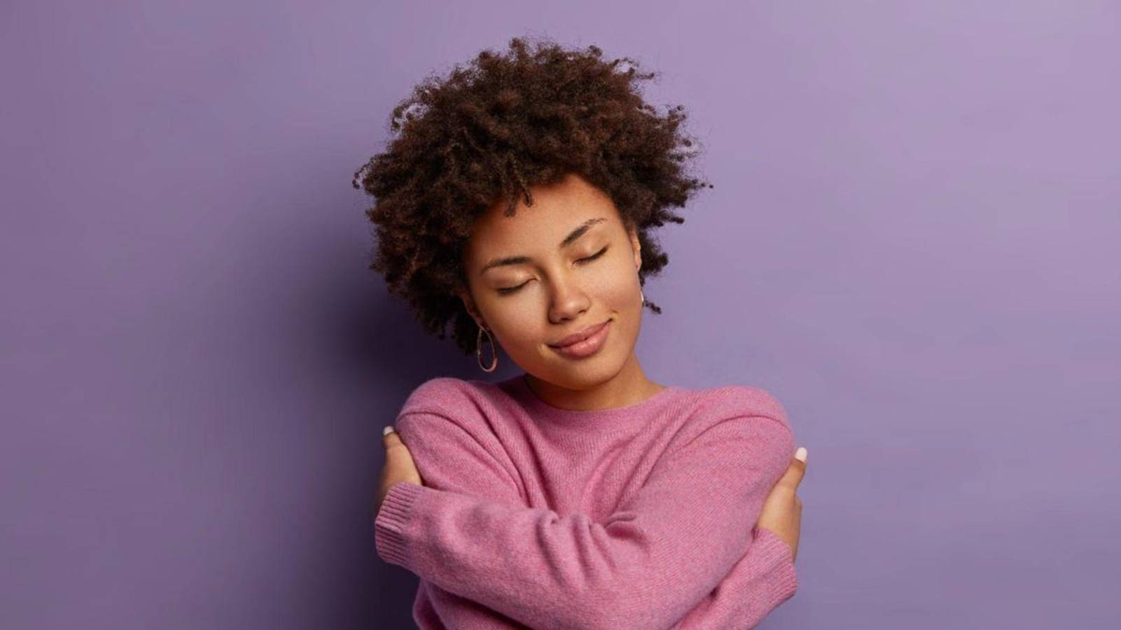 Mulher com suéter em frente a parede com fundo lilás - Março Lilás