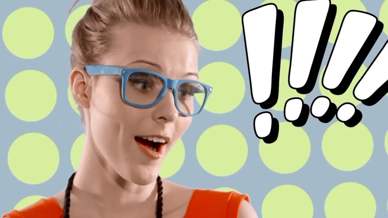 A modern stainless steel Cusimax espresso machine sits on a wooden kitchen counter, with a person holding a white coffee cup in the background, next to a plate with a pastry and a glass of espresso.