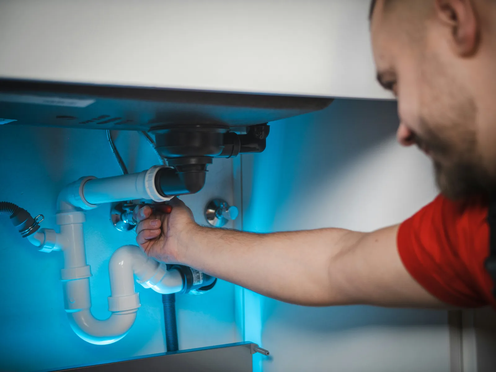 Plumber tightening sink trap pipe connections under cabinet with blue light