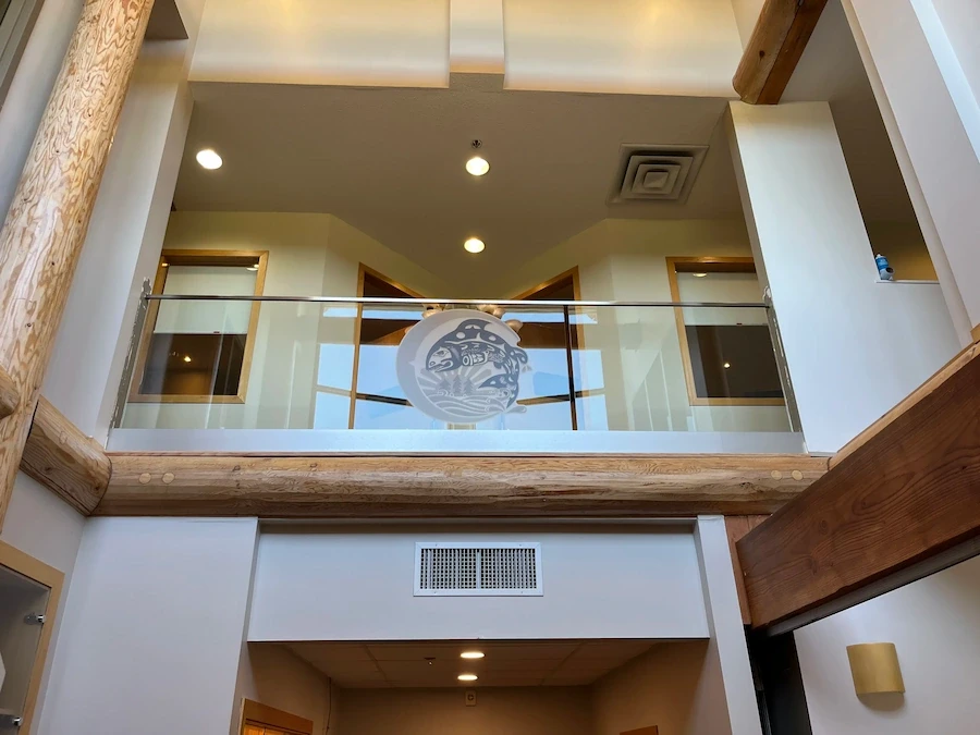 Interior glass railing with etched Indigenous artwork in a modern lobby featuring natural wood beams and warm lighting.
