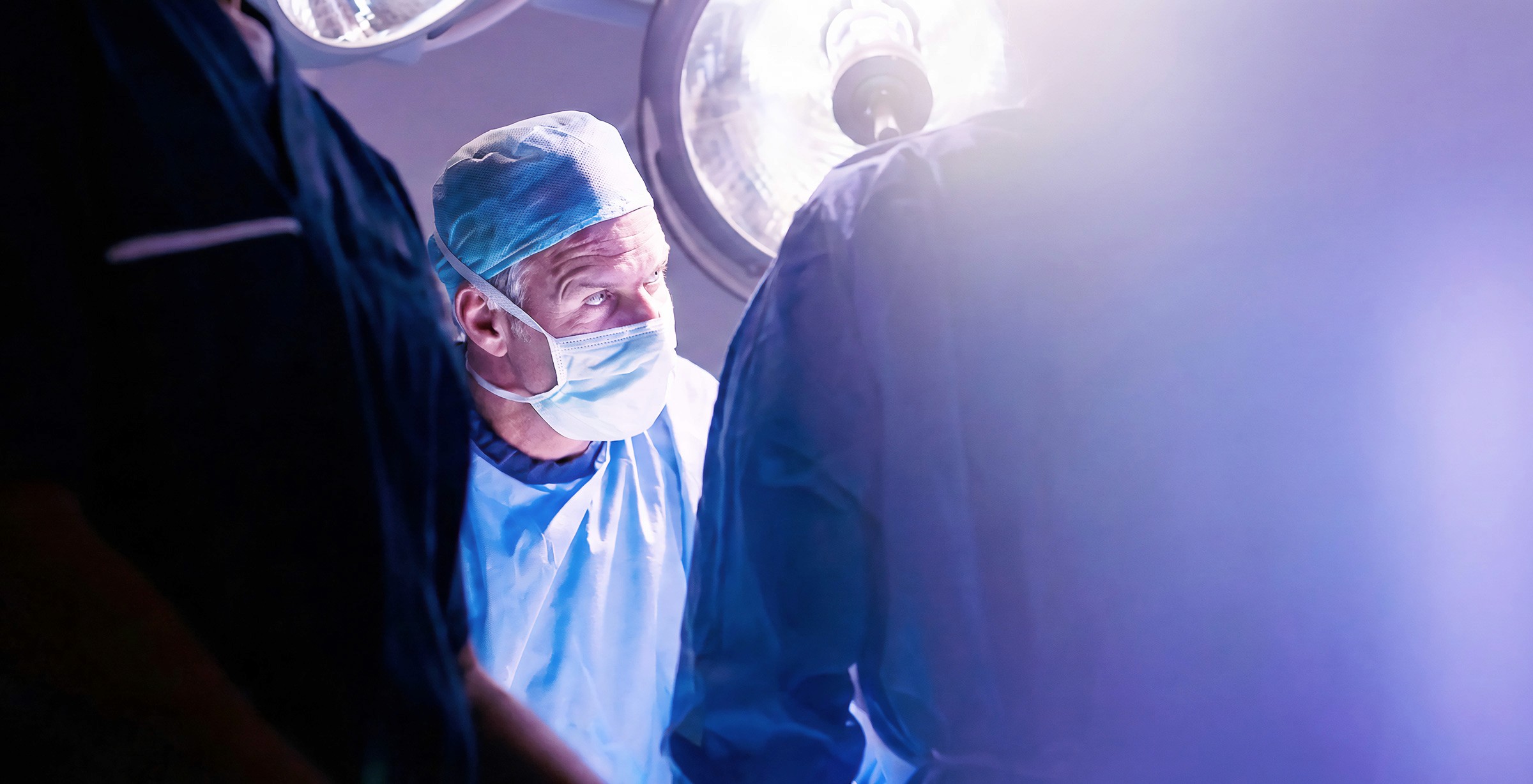 Close-up of a scientist holding a tray of petri dishes with purple cultures, wearing gloves and safety gear.