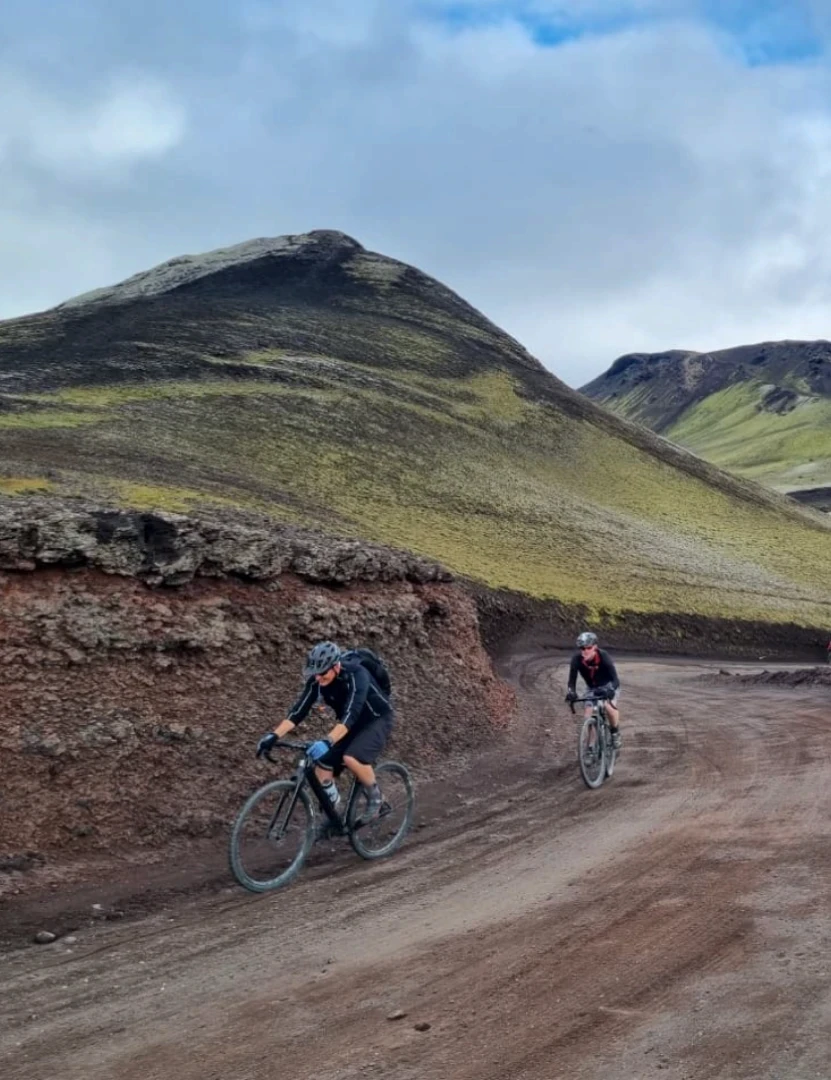 two cyclists ride towards camera with landscapes in backround
