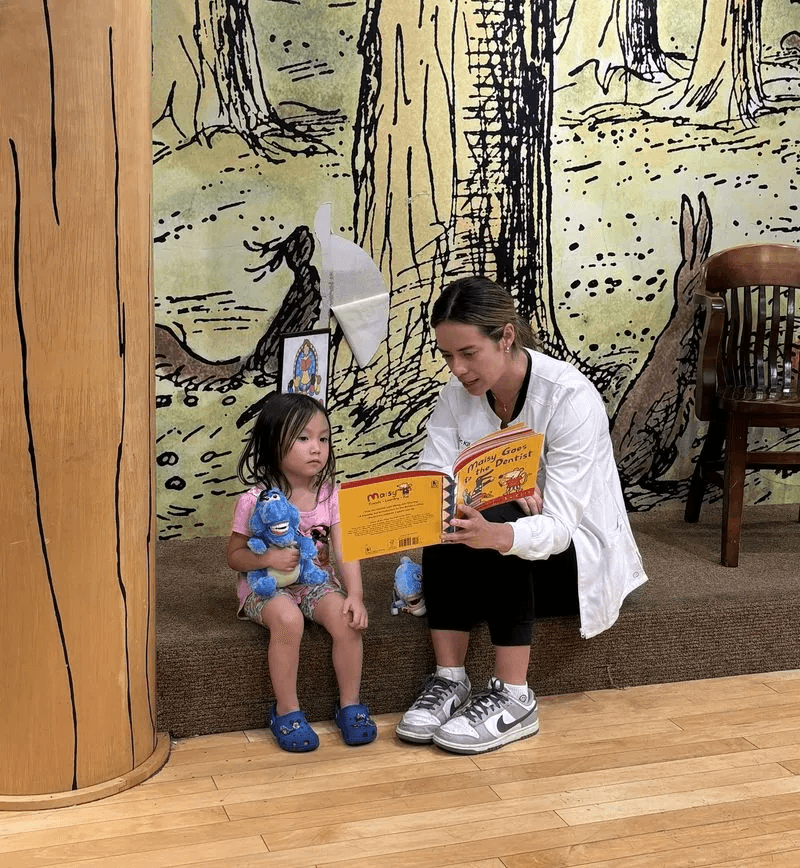 A pediatric dentist sitting with a young child, reading a book together in a child-friendly dental office