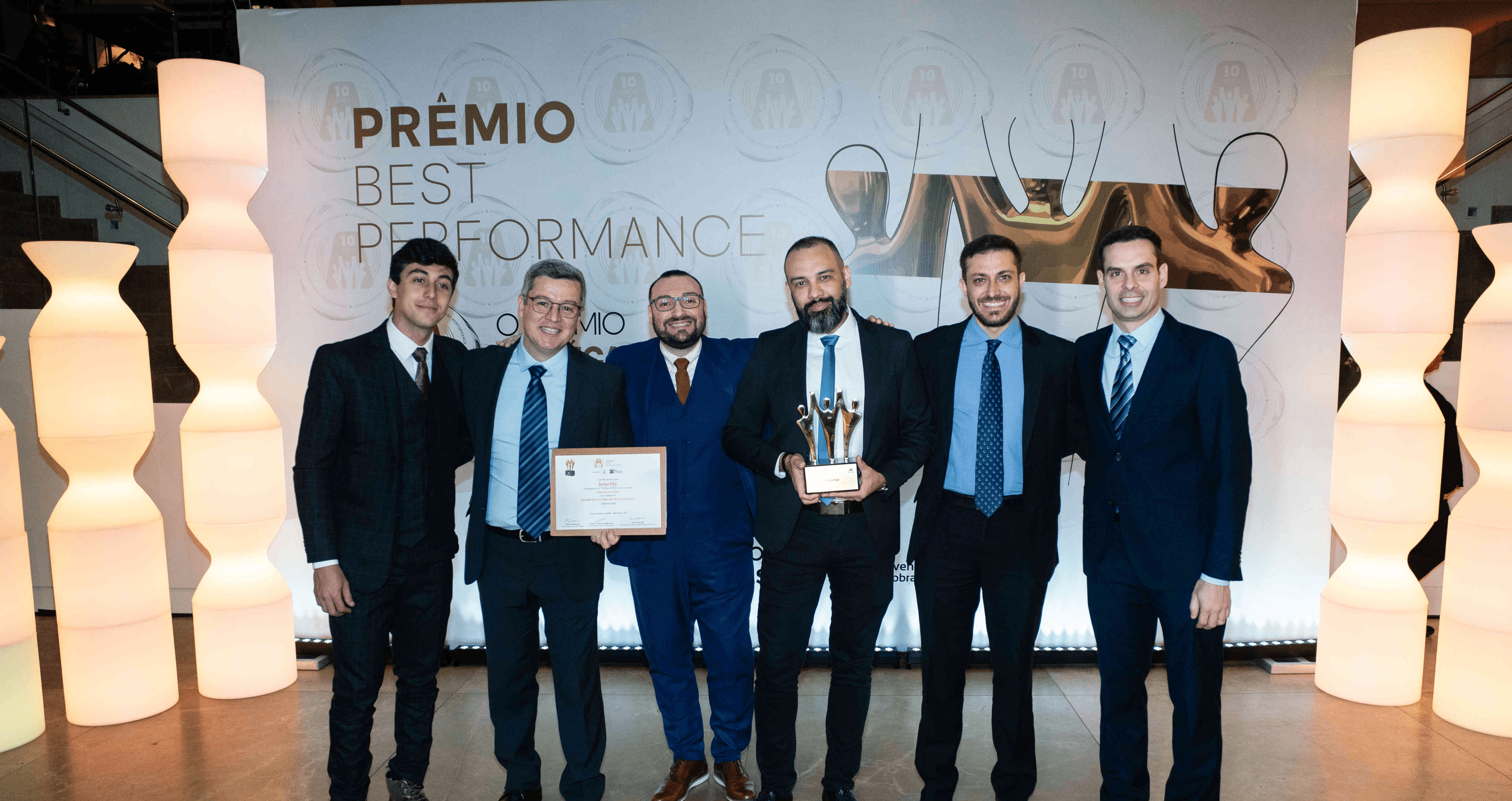 Executivos da Interfile posando com troféu ouro e certificado no palco do Prêmio Best Performance 2025
