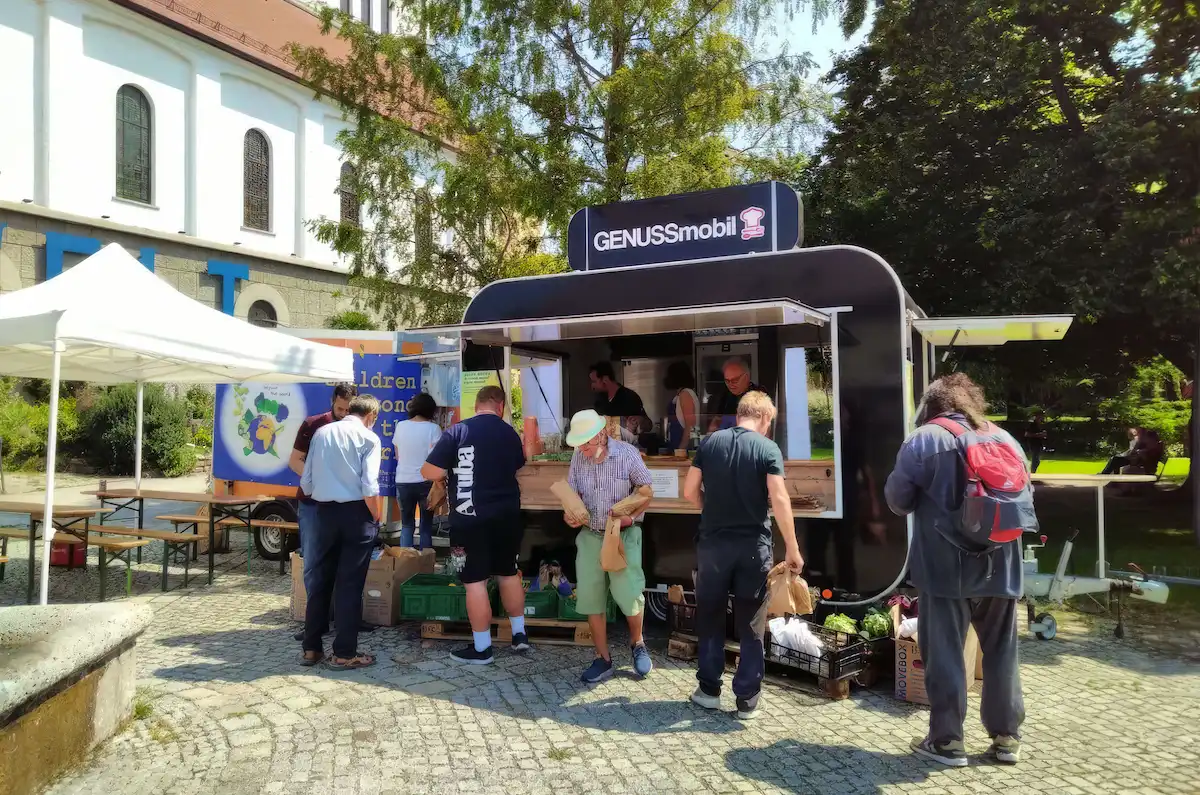 Ein mobiler Foodtruck ('GENUSSmobil') versorgt Menschen im Freien mit veganen Mahlzeiten.