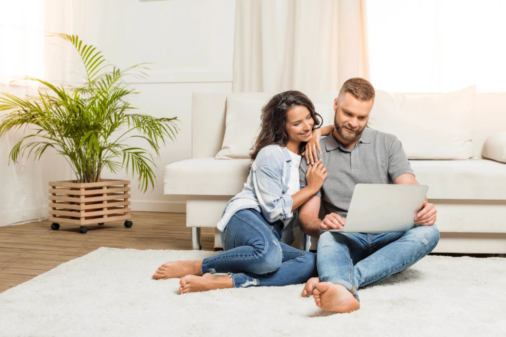 Happy couple sitting on floor browsing on laptop.