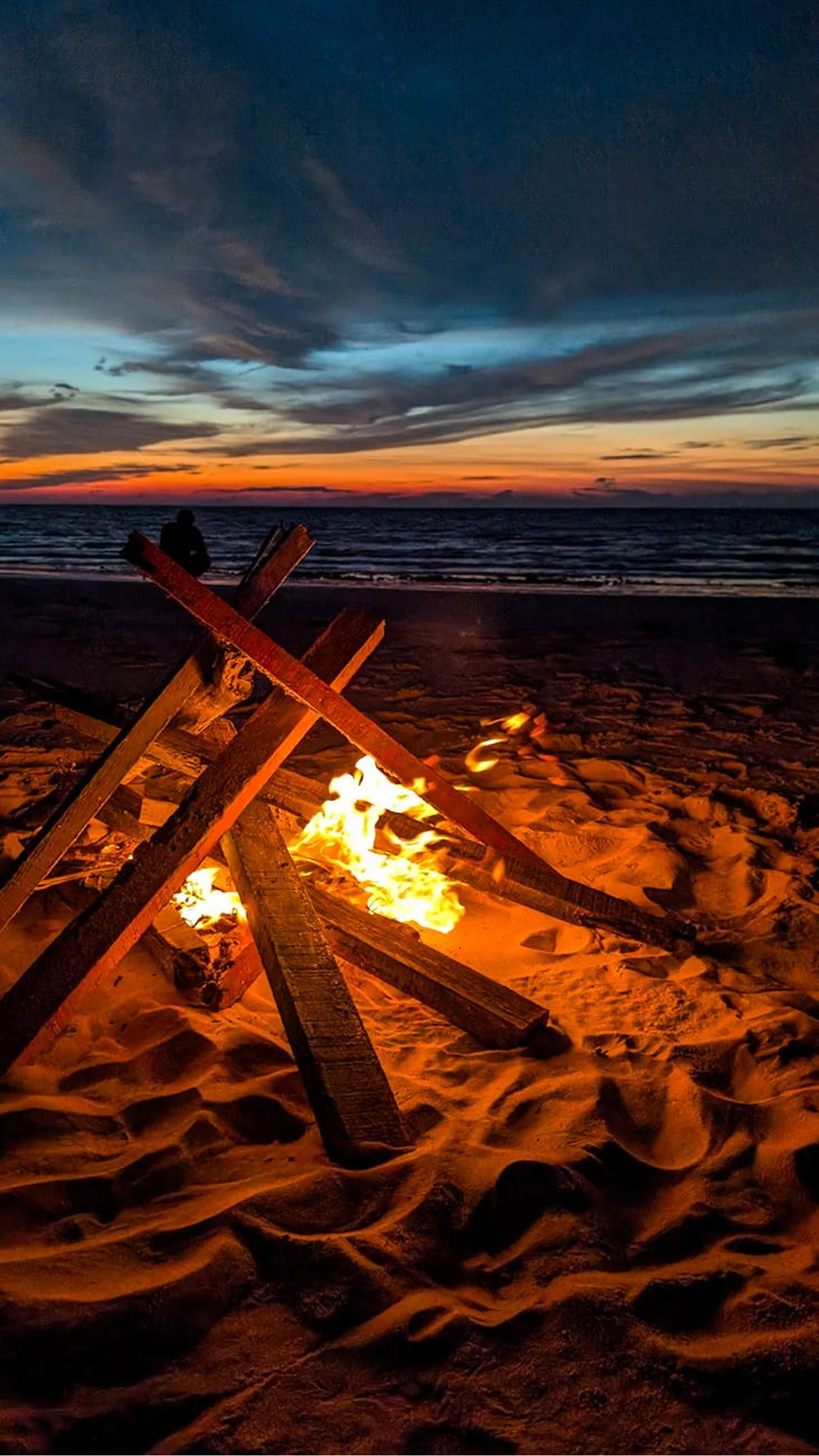 Beach bonfire glowing on the sand at sunset by the sea.