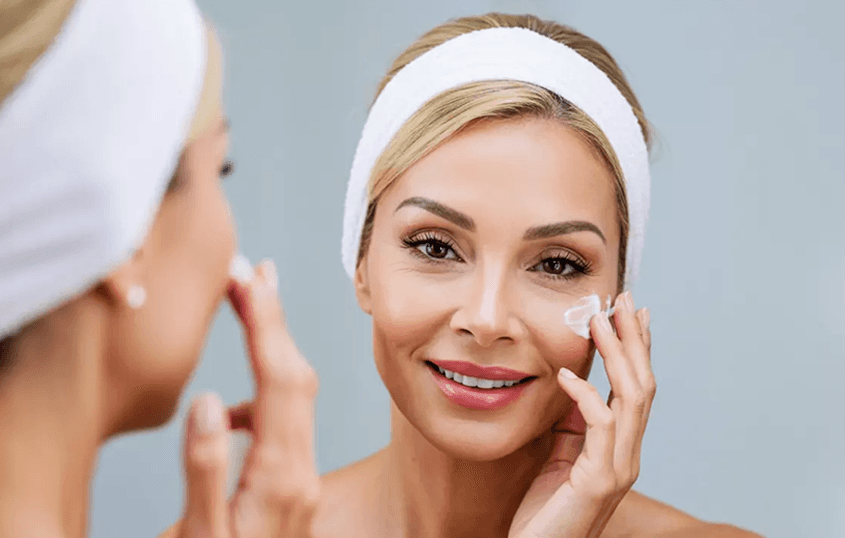 Woman applying anti-wrinkle cream to her face in front of a mirror, illustrating how PureFlow complements a nighttime skincare routine by reducing friction while skincare products remain on the face.