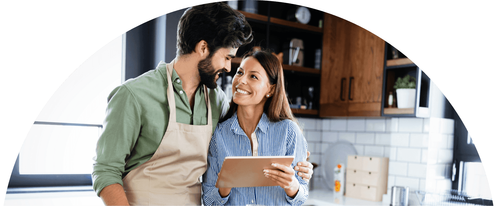 Couple stands close together in a modern kitchen smiling at each other while holding a tablet