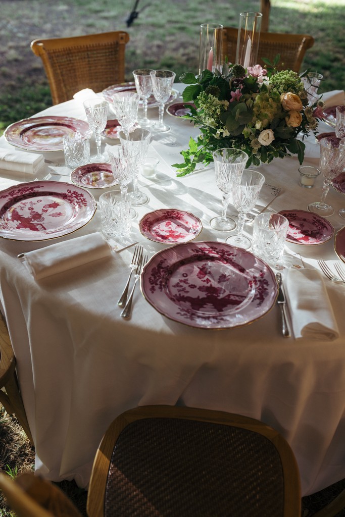 Tavolo di ricevimento matrimoniale con piatti bordeaux, bicchieri cristallo e centrotavola floreale in stile romantico