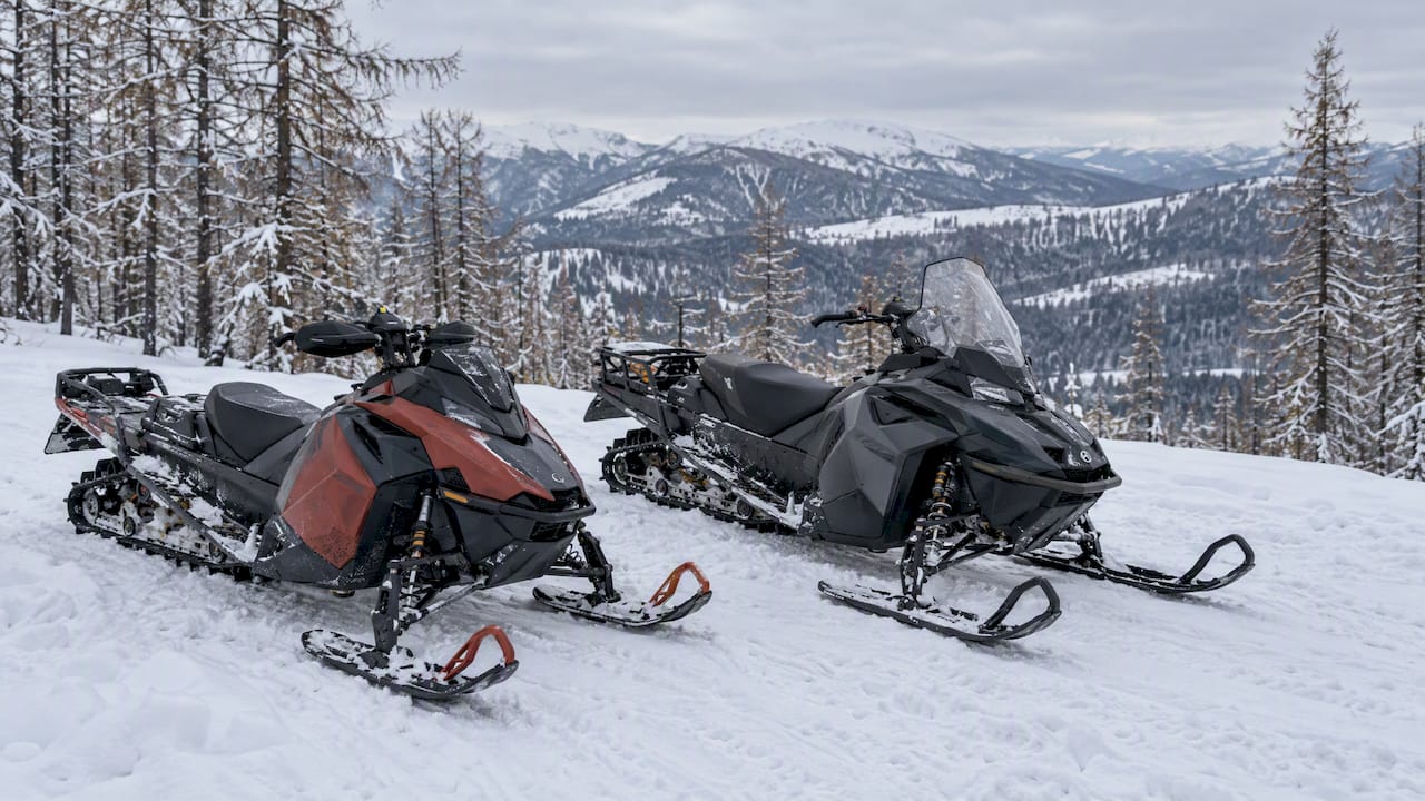 Two snowmobiles parked on a snow-covered open slope in the Western Altai
