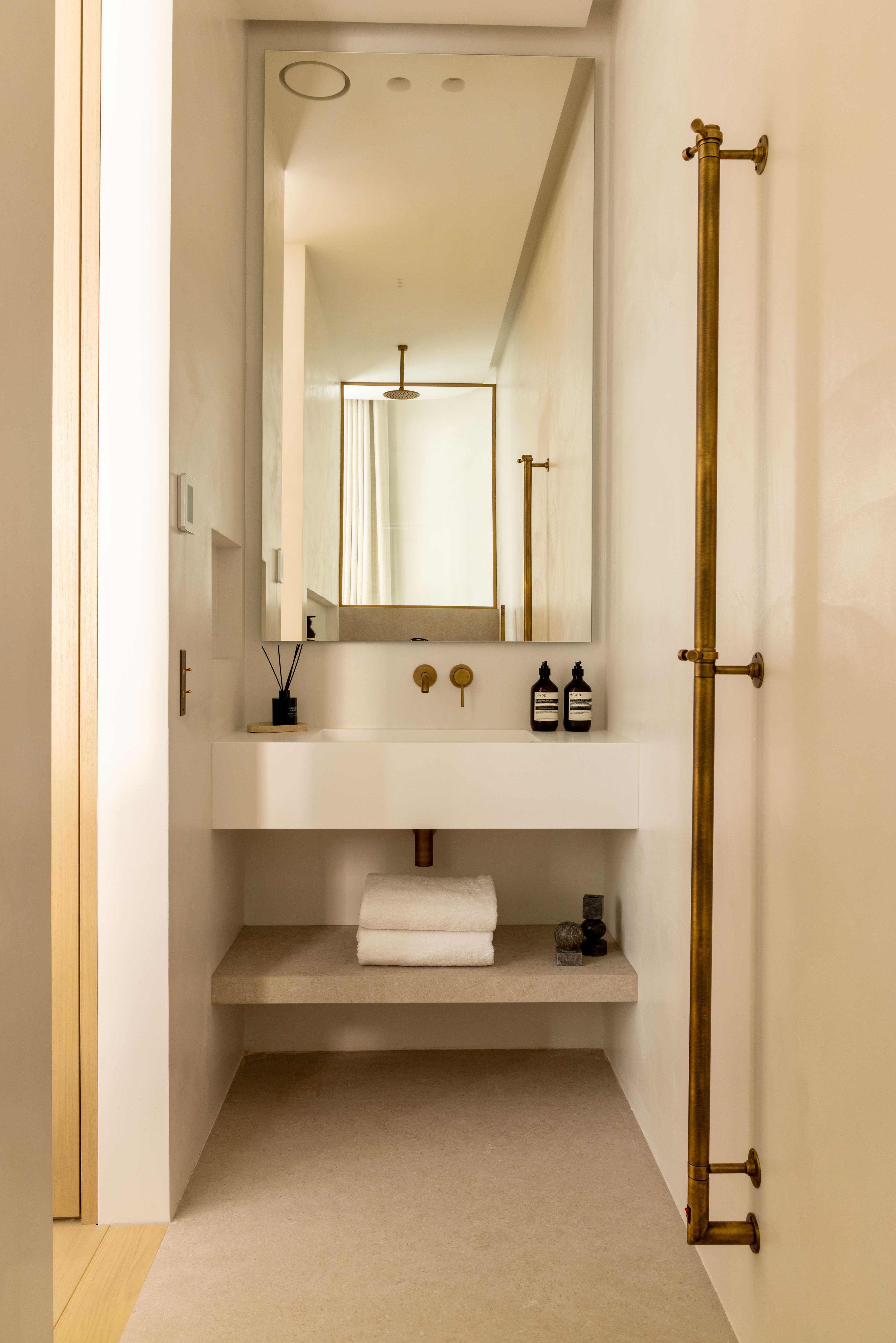 Salle de bain avec vasque suspendue blanche, miroir dore, robinetterie doree et porte-serviettes en laiton