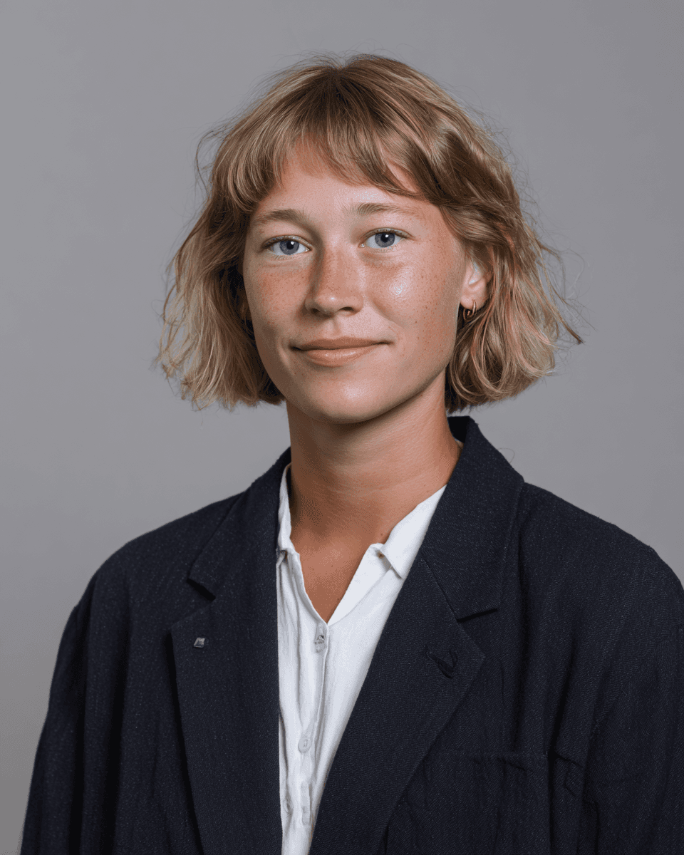 A man with dark curly hair and glasses smiling in a portrait.