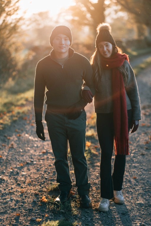 A couple facing the camera walking down a country lane at golden hour.