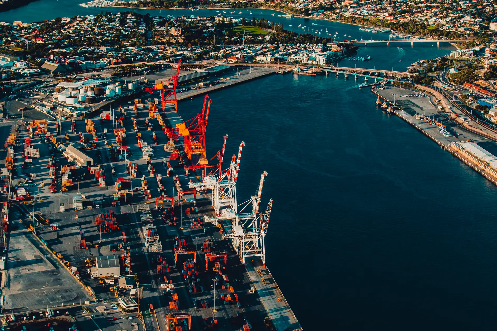 Aerial of a container terminal, red gantry cranes and stacked containers lining a harbour channel