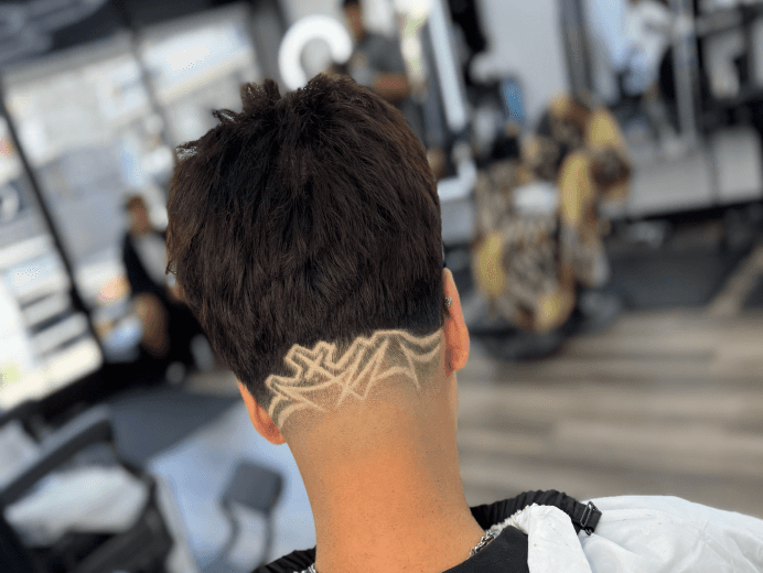 Back view of a man’s haircut featuring a fade with a detailed hair design shaved into the lower section.