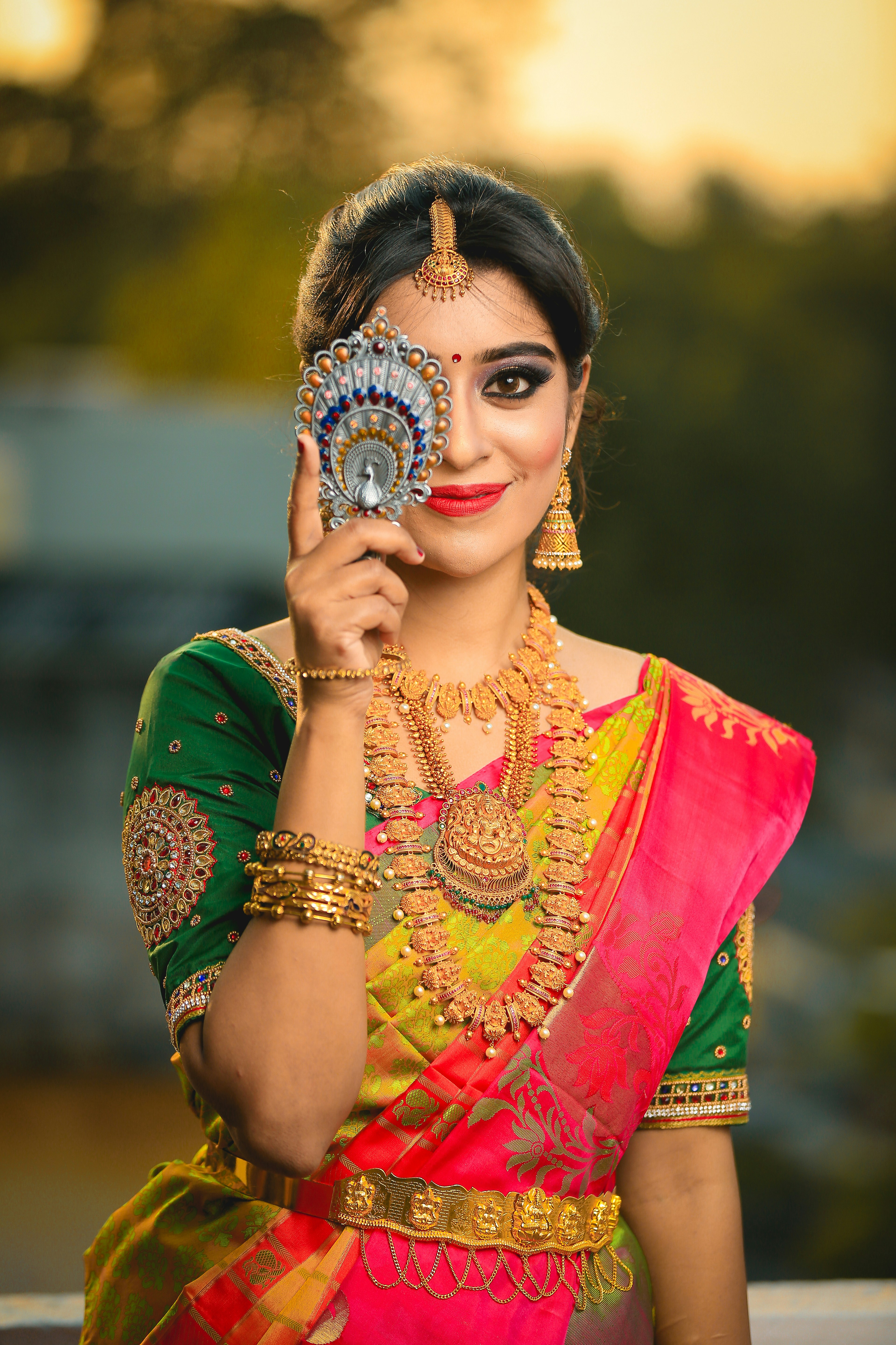 woman in green, gold, and red sari dress hiding her right eye while smiling