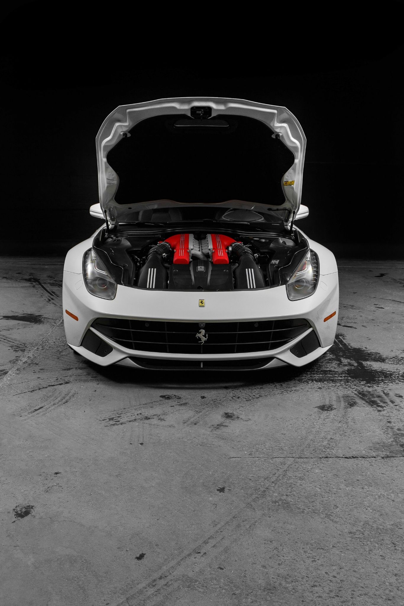 A sleek, white sports car with its hood open reveals a powerful, red-highlighted engine, set against a dark backdrop, emphasizing its luxurious and high-performance design.