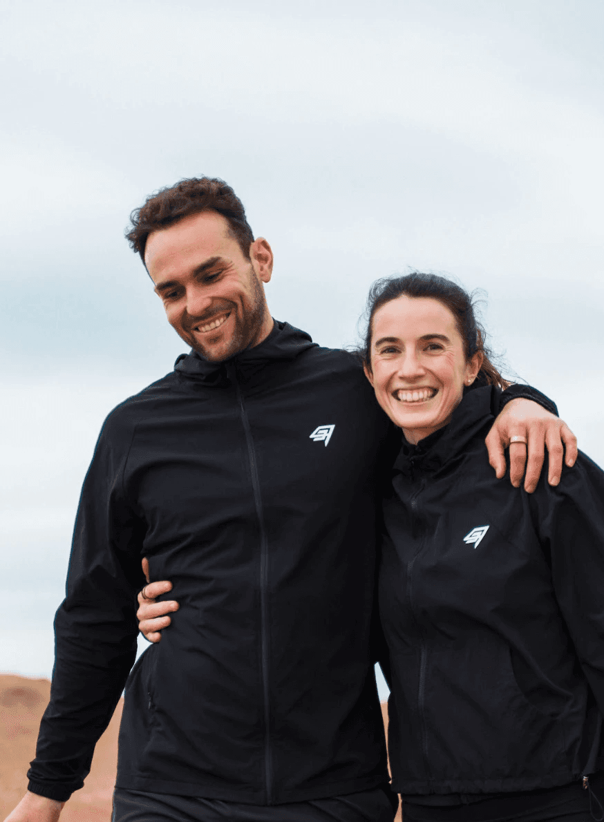 Dynamic close-up of a runner’s foot mid-stride on a muddy forest trail, wearing black socks and red trail shoes with visible sole pattern.
