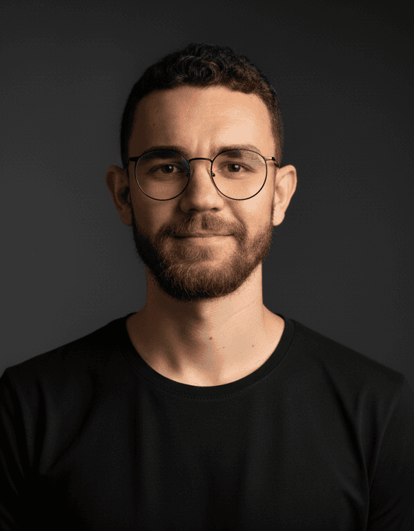 Close-up portrait of a person wearing a gray insulated hooded jacket with the hood up, showing their face framed by the hood against a light background.
