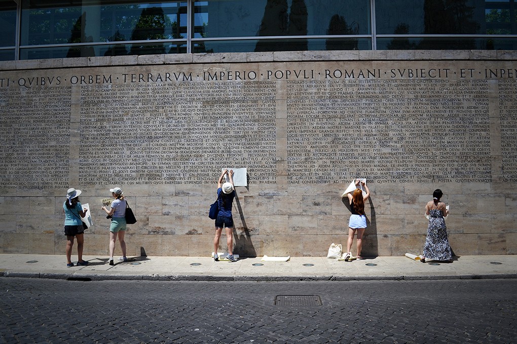 students shaving the graphite pen to a paper and put over an engraved text on the wall