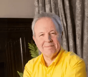 Professional photo of Kevin Wright wearing a yellow shirt, seated and smiling at camera