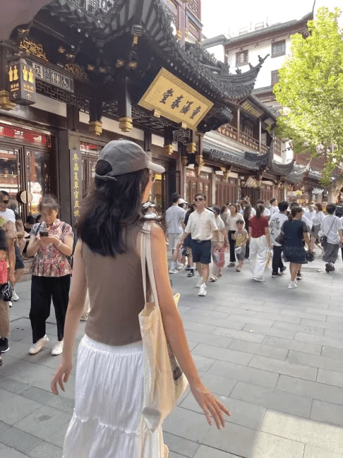 Una persona con una camiseta negra y pantalones de color claro está de pie en la cima rocosa de una montaña al atardecer, sosteniendo una cámara frente a su cara para tomar una foto. Un mar de nubes se extiende detrás de ellos, iluminado por la luz dorada del sol poniente.