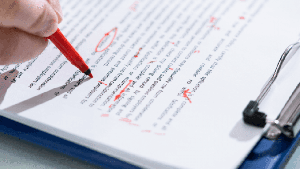 A student reviewing a printed academic paper with handwritten proof correction marks and a red pen on a desk