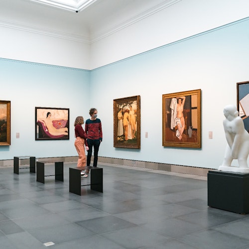 一对夫妇在一个宽敞、阳光充足的艺术画廊里欣赏画作和白色雕塑。