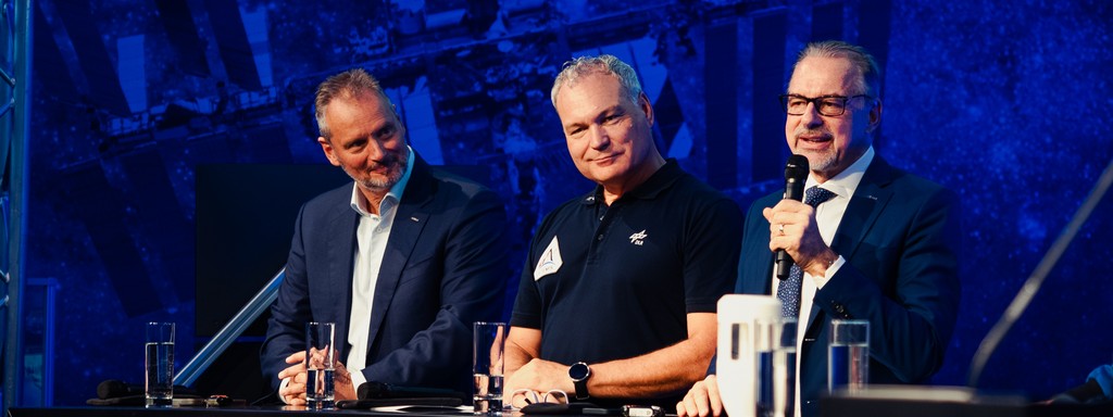Three male speakers standing side by side on a stage